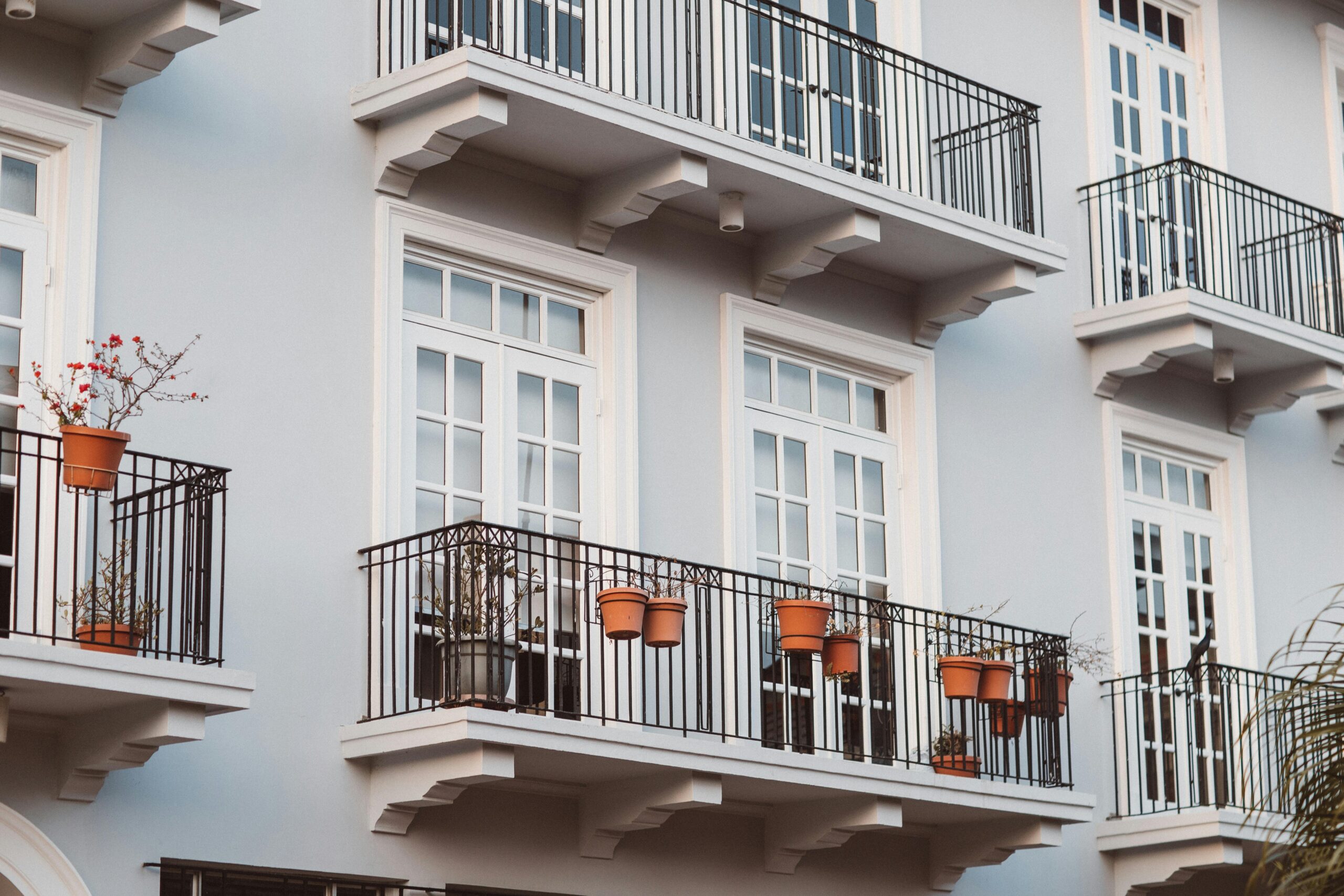 Front view of a modern building with balconies, pots, and white framed windows.